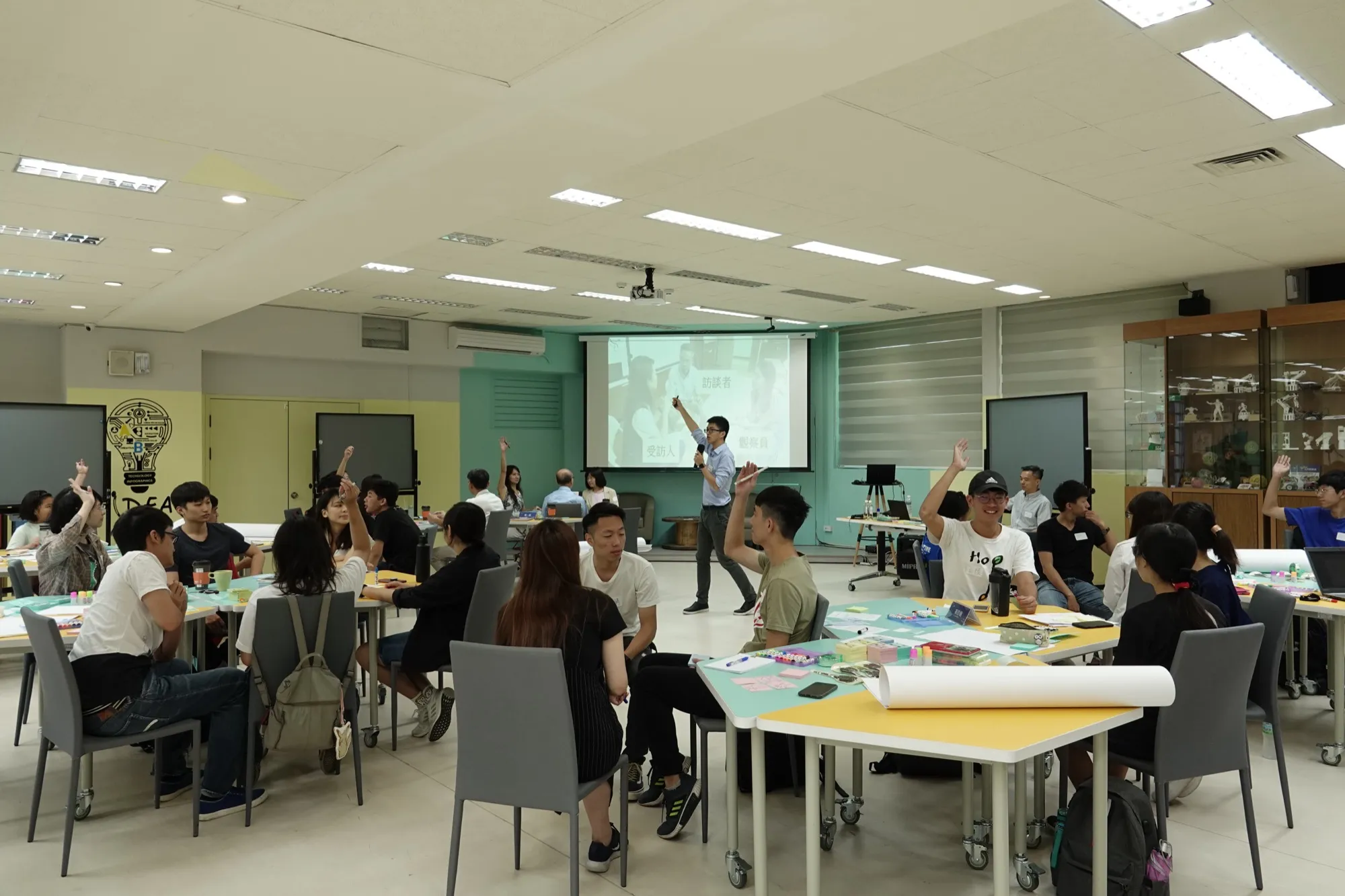 喬在工作坊前方帶活動，各組學員圍著桌子討論